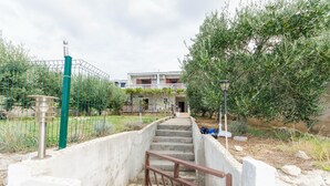 A staircase leading to a building with a balcony, surrounded by greenery and a fence. - Apartments Seafront Jadranka (Novalja)