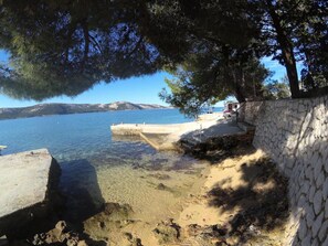 A coastal scene with clear water, a stone wall, and a small pier. - Apartments Seafront Jadranka (Novalja)
