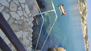 A stone-paved area leading to a clear blue sea with a boat anchored nearby. - Apartments Seafront Jadranka (Novalja)