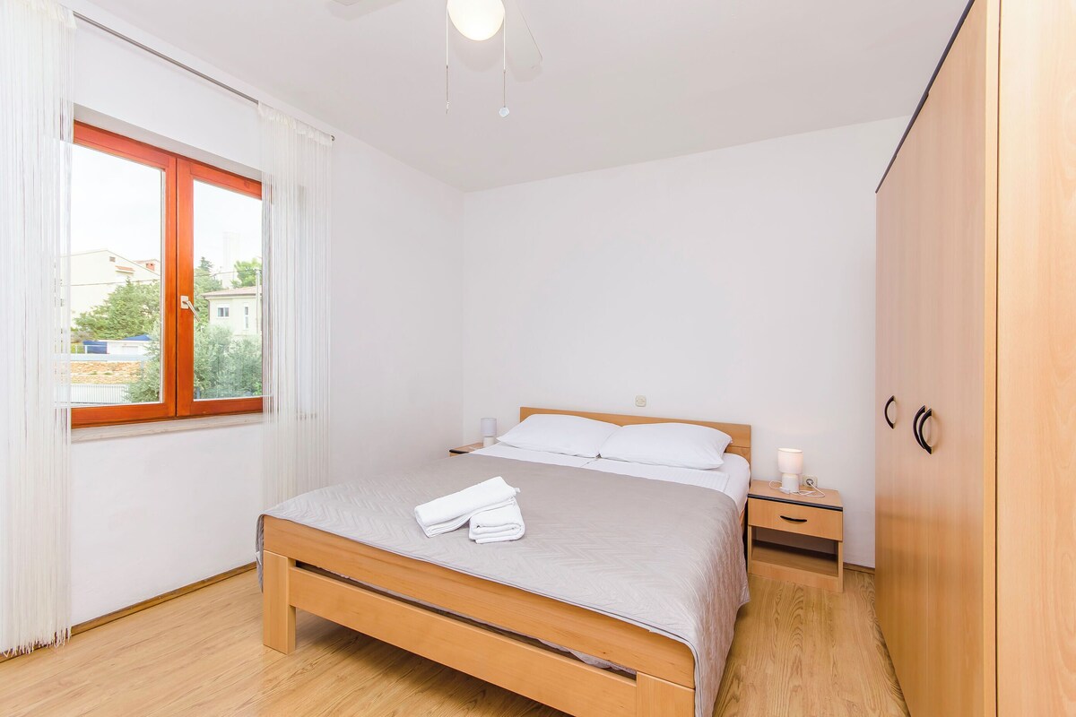 A bedroom with a wooden bed, a bedside table with a lamp, a wardrobe, and a window with curtains.