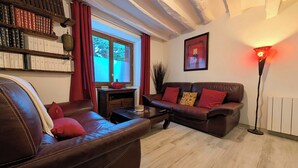 A cozy living room with leather sofas, a bookshelf, a red vase, and a floor lamp. - Maison Cévenole - Village center - Flexible arrival (Saint-Jean-du-Gard)
