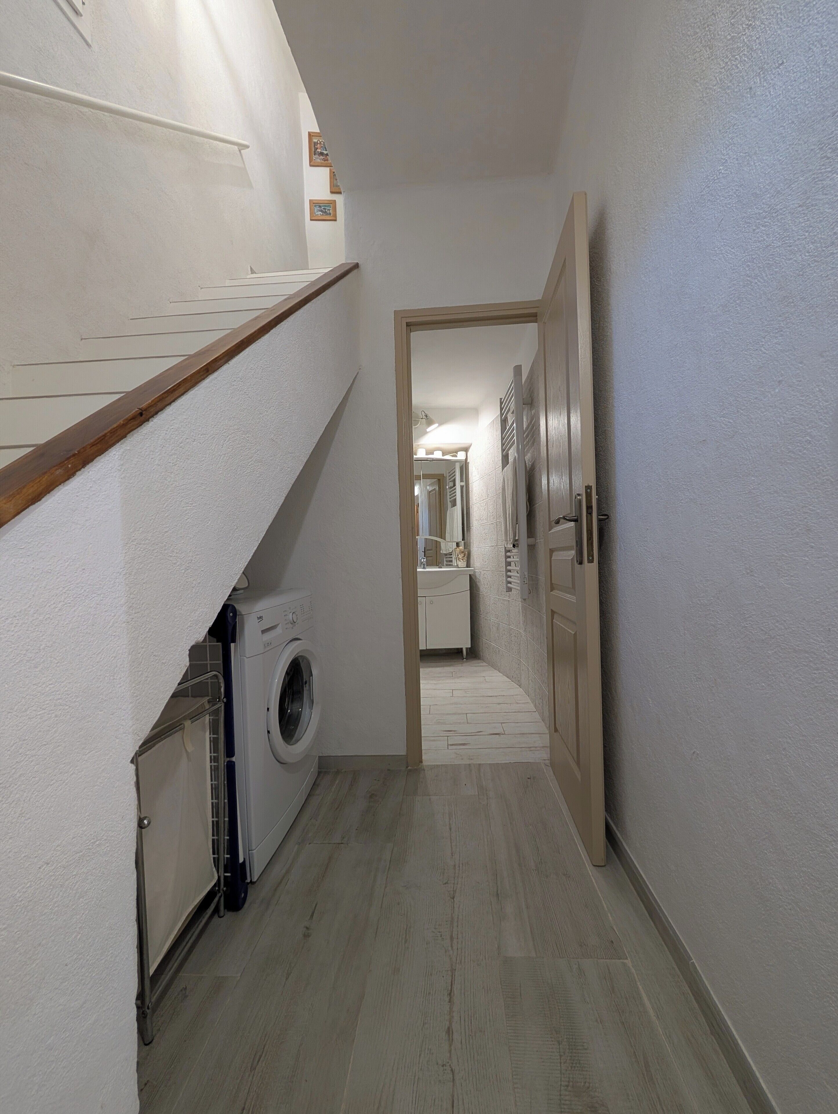 A narrow hallway with a washing machine and a wooden staircase.