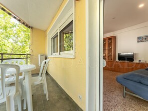 Et værelse med balkon, et spisebord med stole, en sofa, et fjernsyn og et skab med service.