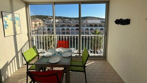 Un balcon avec une table dressée pour quatre personnes, offrant une vue sur un paysage urbain avec des immeubles et une colline.
