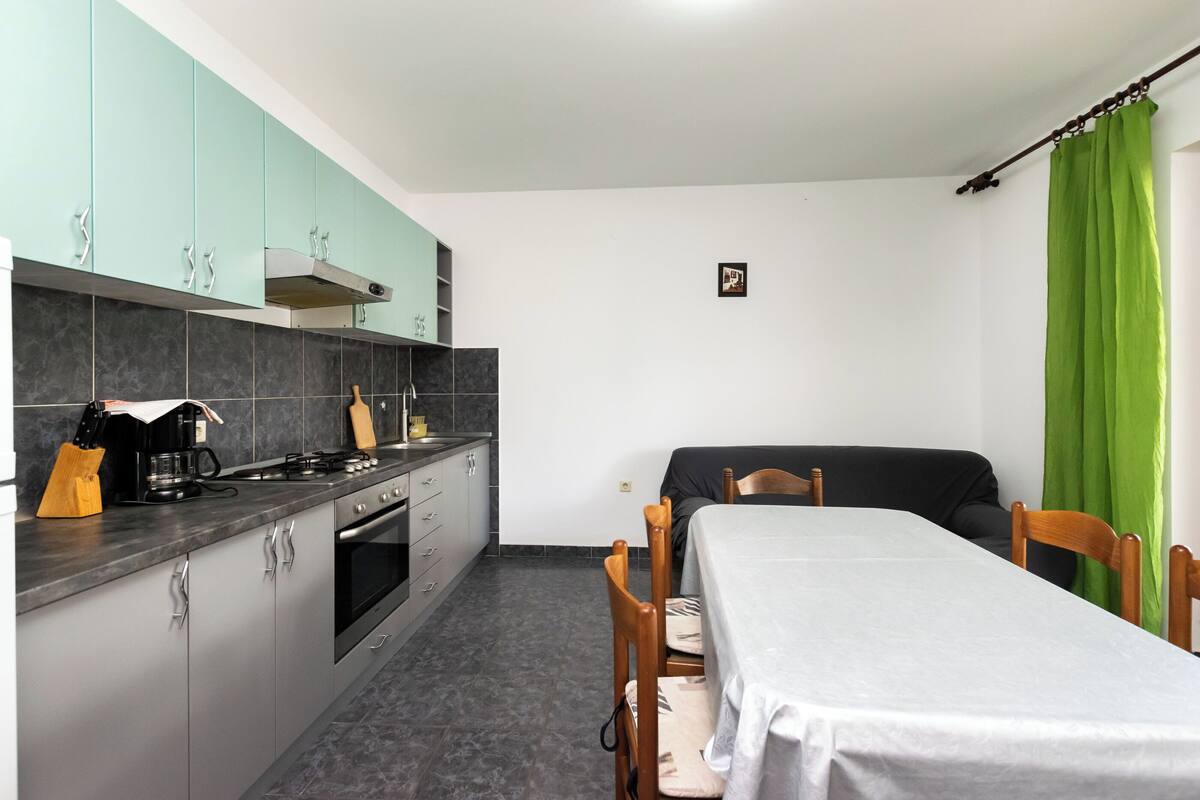 Une cuisine compacte avec des meubles gris, une cuisinière et un coin repas comprenant une table et des chaises.