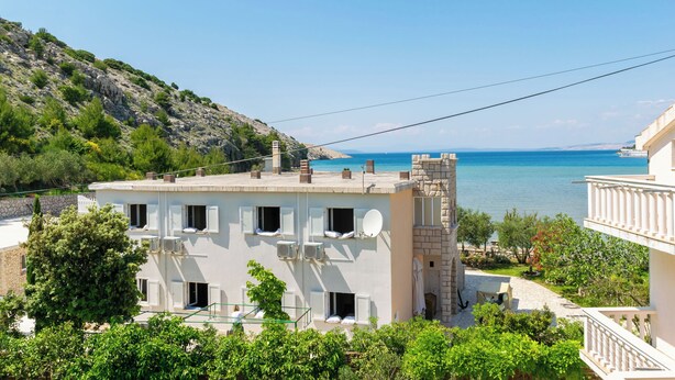Un bâtiment situé sur la côte, doté de nombreuses fenêtres et d’un balcon, qui offre une vue sur une mer bleue et limpide.