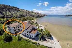 Ein Küstenanwesen mit einem zweigeschossigen Gebäude, einem Strand und einer felsigen Hügelkuppe.