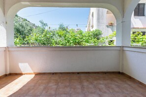 Ένα δωμάτιο με πλακάκι στο δάπεδο, λευκούς τοίχους και ένα παράθυρο με θέα σε έναν κήπο με δέντρα και ένα κτίριο στο βάθος.