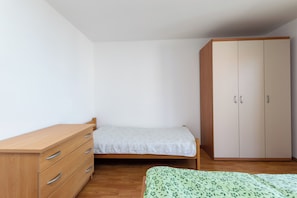 Una camera da letto con un comò in legno, un letto singolo con copripiumino a fiori verdi e un armadio capiente.