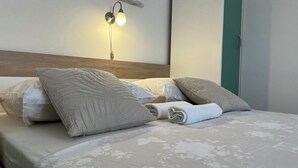 Ein ordentlich bezogenes Bett mit einem blumigen Überwurf, mehreren Kissen und einer Wandleuchte.