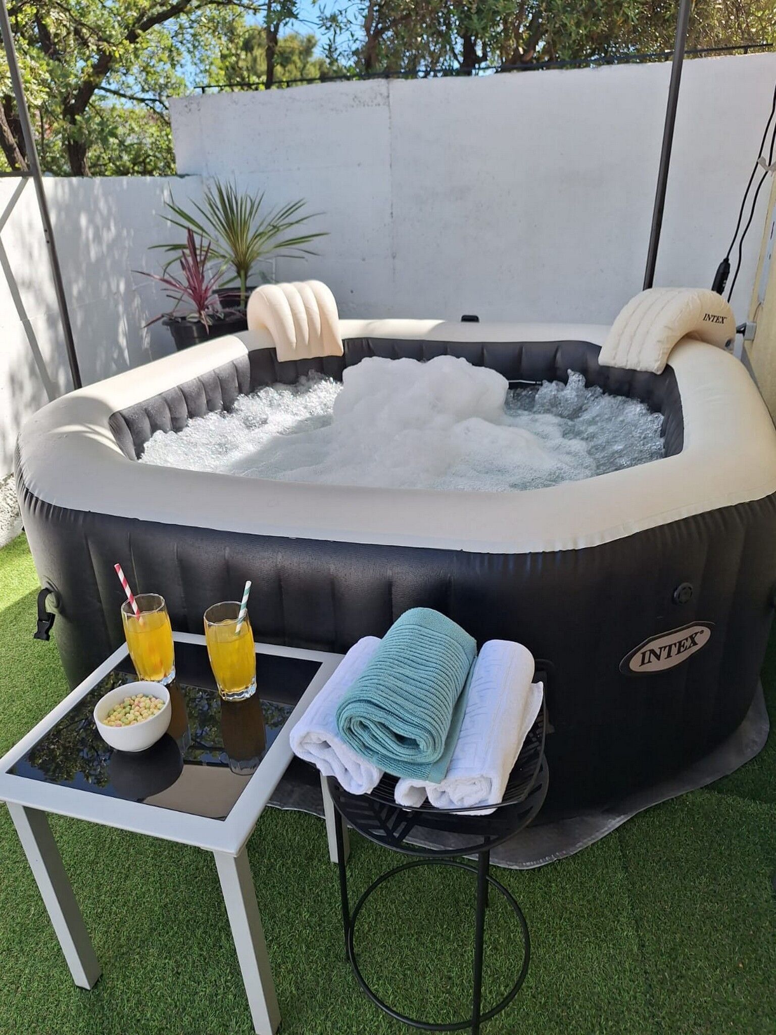 Ein aufblasbarer Whirlpool mit Kissen, ein Tisch mit Getränken und Handtüchern, sowie eine kleine Schale mit Snacks.