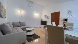 Ein modernes Wohnzimmer mit einer Couch, einem Fernseher, einem Esstisch mit Stühlen und einer Küchenzeile mit Kühlschrank.