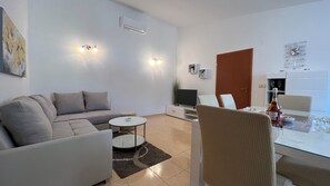 Ein modernes Wohnzimmer mit einer Couch, einem Fernseher, einem Esstisch mit Stühlen und einer Küchenzeile mit Kühlschrank.