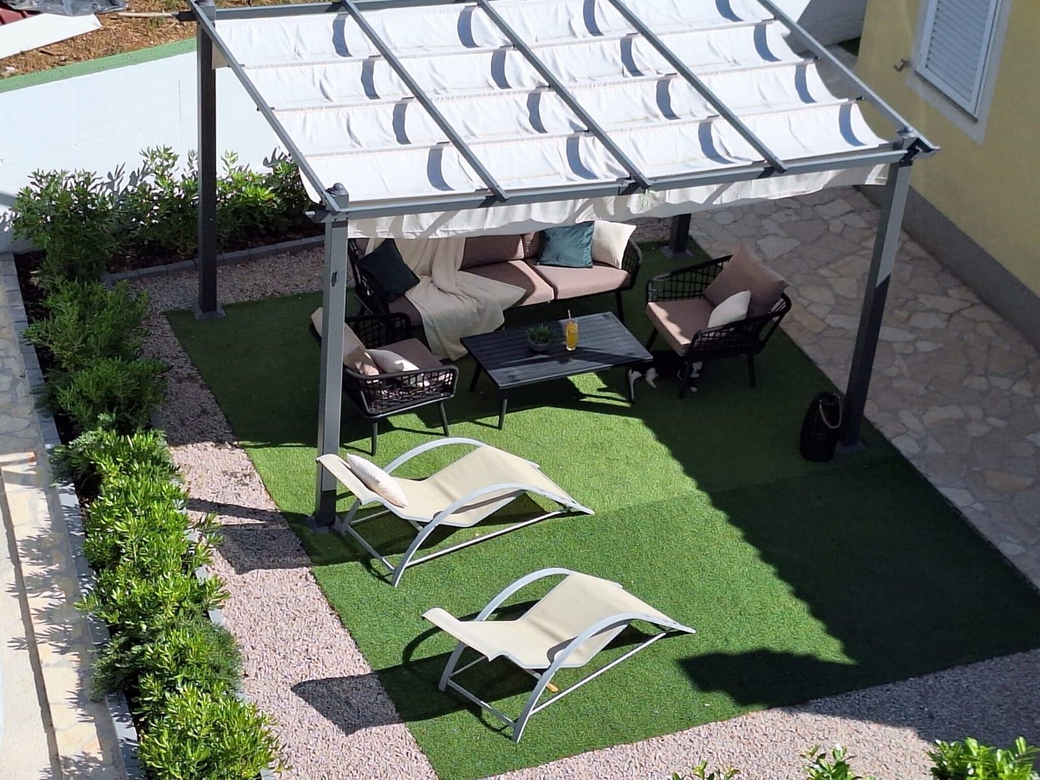 Un área de estar al aire libre con techo, pared de piedra, césped artificial verde y sillones reclinables.
