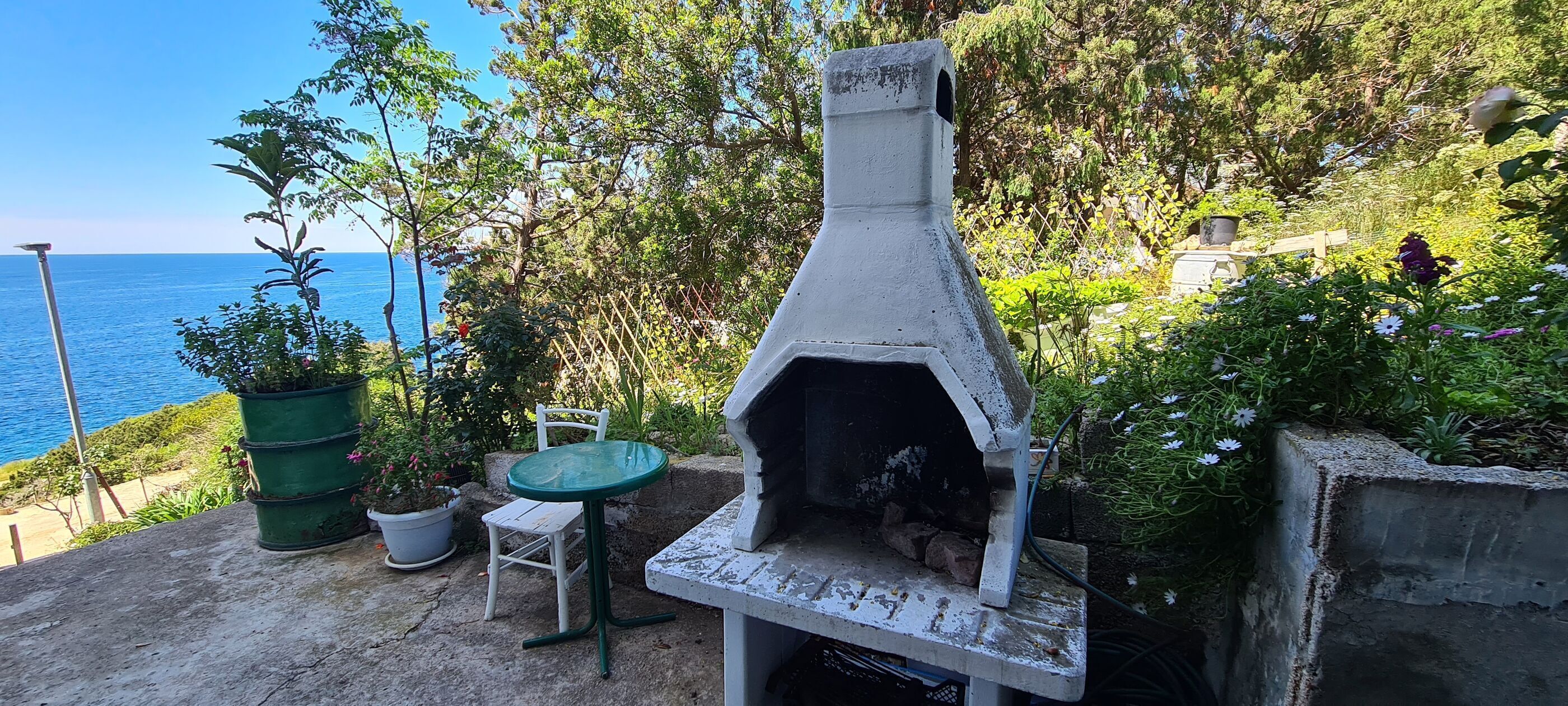 An outdoor patio with a concrete pizza oven, a table, and a chair.