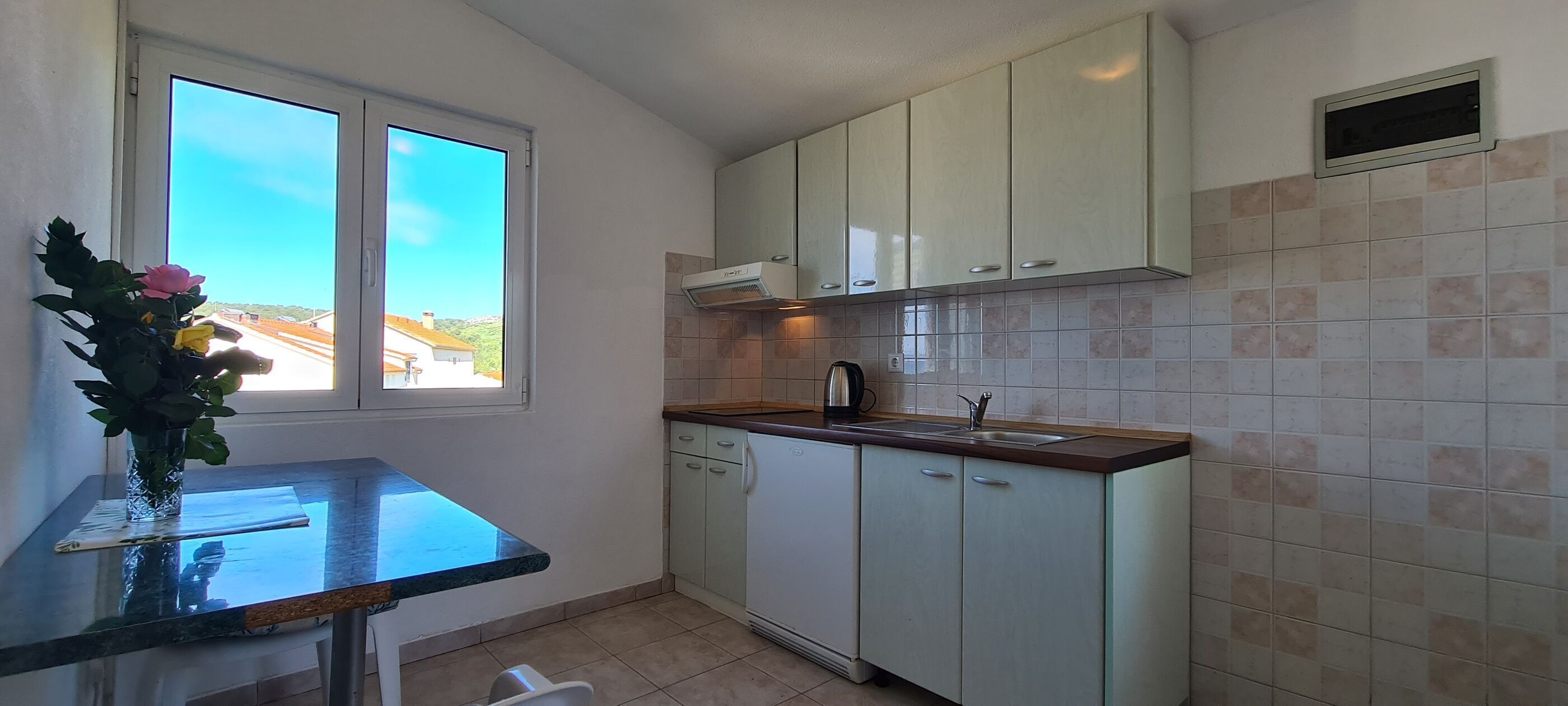 A kitchen with white cabinets, a window with a view, and a countertop with a vase of flowers.