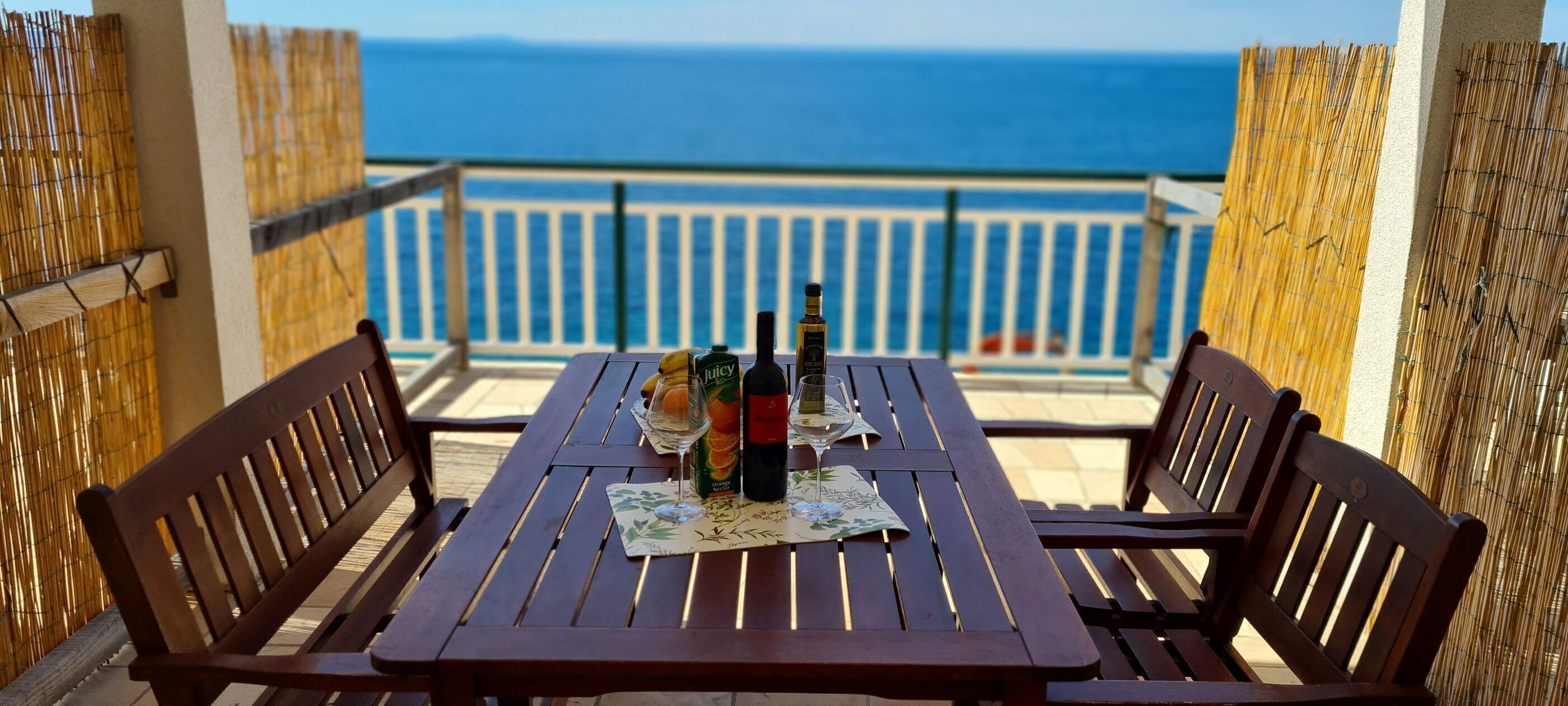 Une table en bois avec deux chaises, sur un balcon donnant sur la mer.