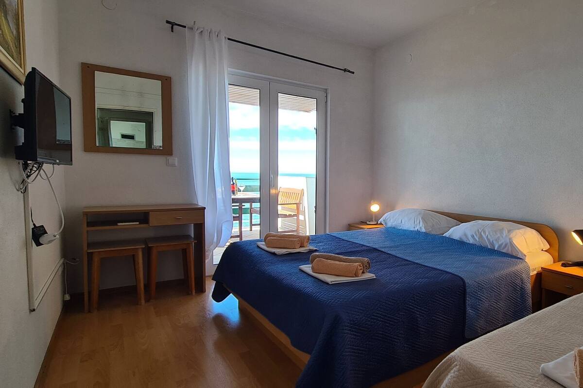 A bedroom with two beds, a desk, and a balcony with a view.