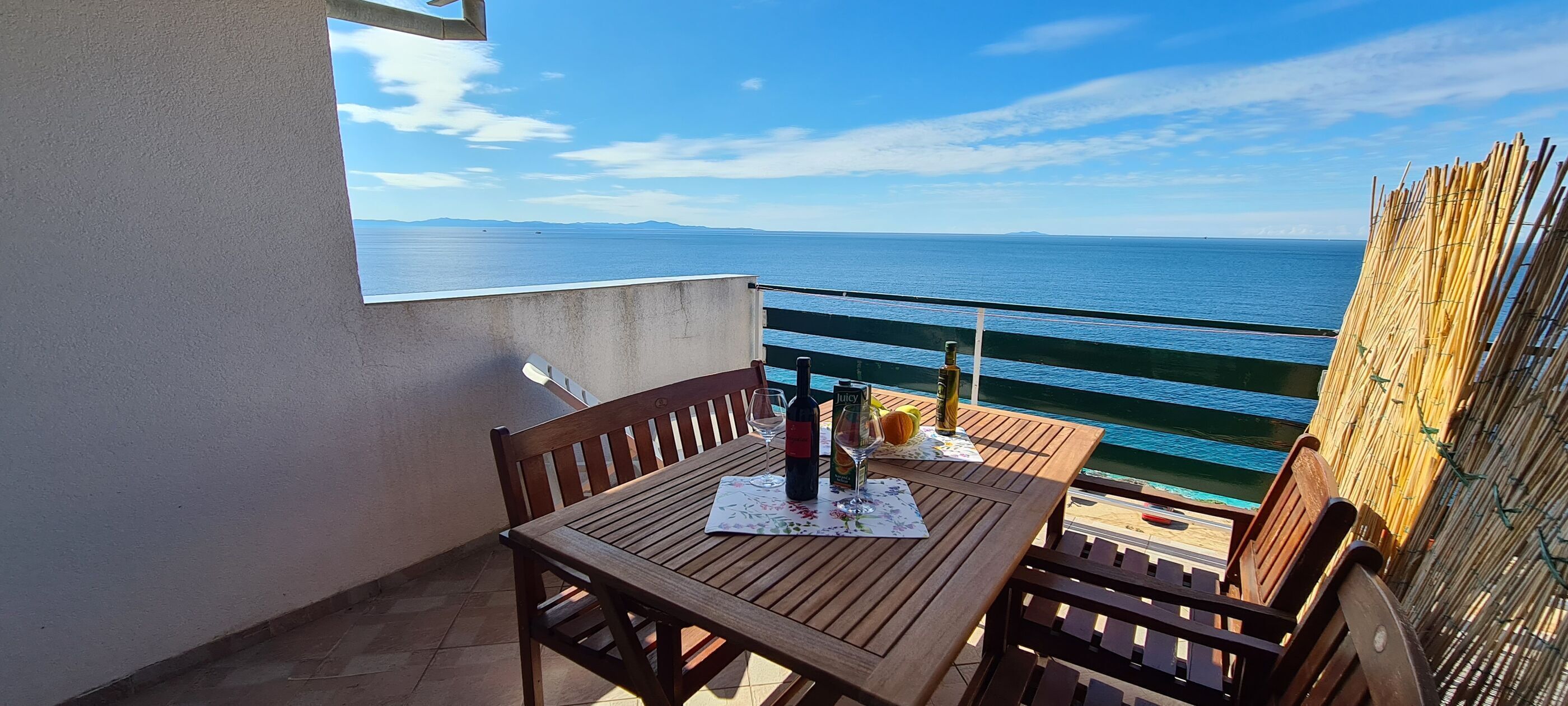A wooden table with a bottle and glass on a balcony overlooking the sea.