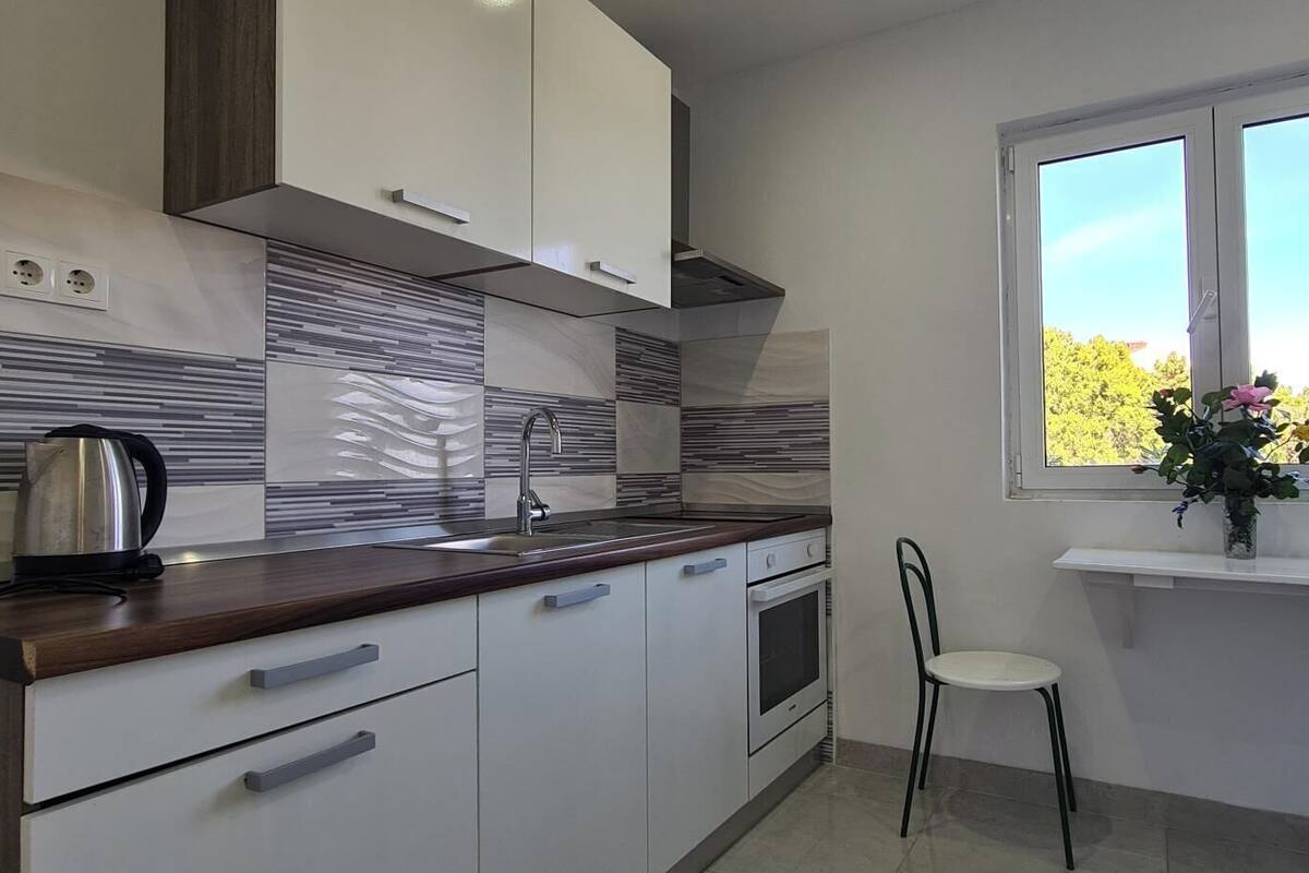 A modern kitchen with white cabinets, a wooden countertop, a kettle, and a window with a view of greenery.