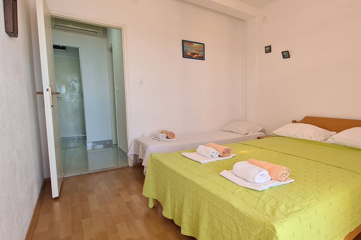 A bedroom with a large bed, two smaller beds, a nightstand with a lamp, and a door leading to a bathroom.