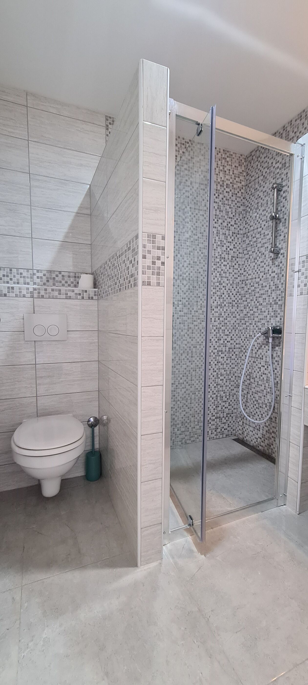 A bathroom with a toilet, a shower with a glass door, and tiled walls.