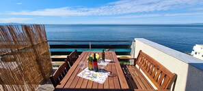 A wooden table with a bottle of wine and glasses, overlooking a calm sea. - Apartments Ana i Ante Punta (Hvar)