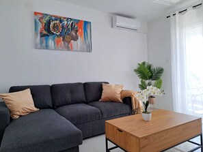 En moderne stue med en grå hjørnesofa, et træ sofabord og en potteplante.