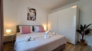 A modern hotel room with a large bed, two bedside tables, a wardrobe, and a potted plant. - Apartment Beach View (Crikvenica)