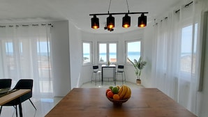 A spacious dining area with a wooden table, a fruit bowl, and a view of the sea through large windows. - Apartment Beach View (Crikvenica)