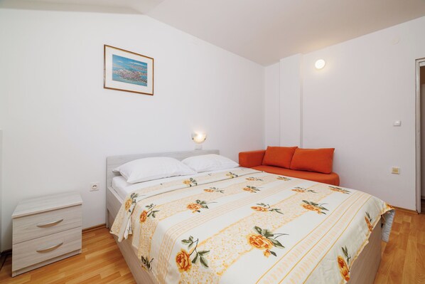 Une chambre à coucher avec un lit, une table de chevet, une lampe de chevet, un canapé orange et un tableau encadré au mur.