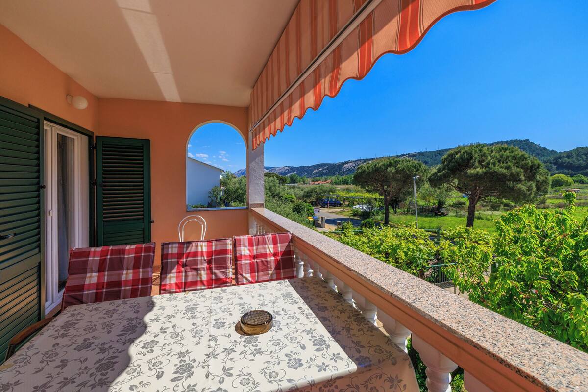 Ein Balkon mit Tisch und Stühlen, Blick auf eine grüne Landschaft und ein Gebäude mit markanter Architektur.