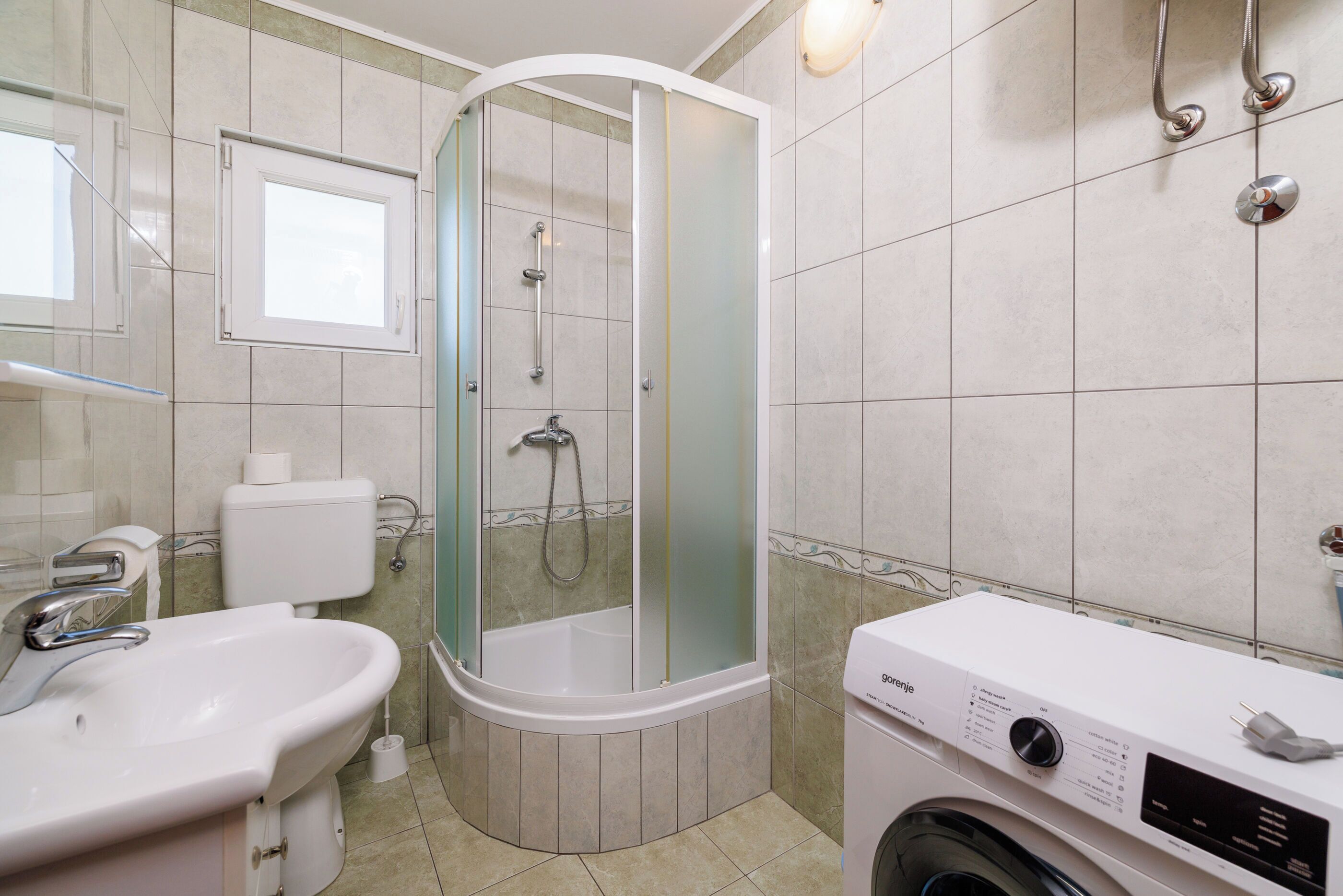 A bathroom with a glass-enclosed shower, a sink, a toilet, and a washing machine.