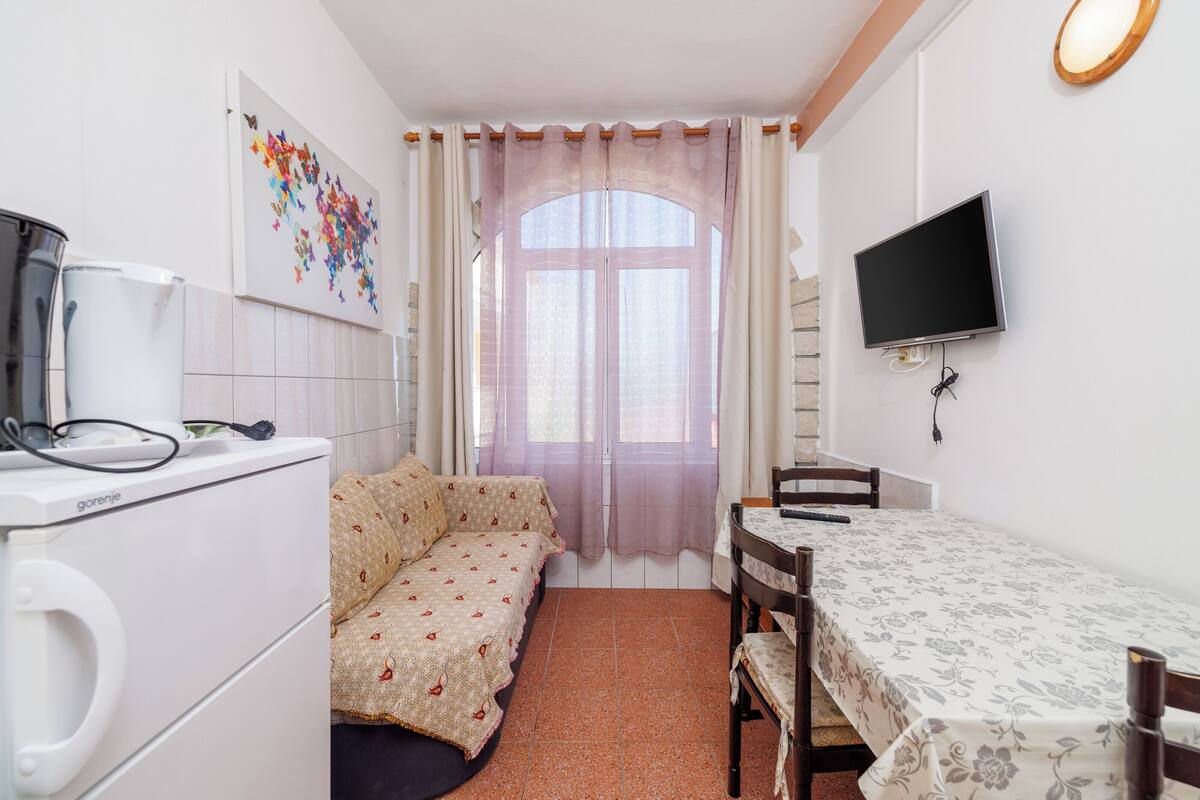 Ein kleines Zimmer mit einem Bett, einem Schreibtisch, einem Stuhl, einem Fernseher und einer Waschmaschine.