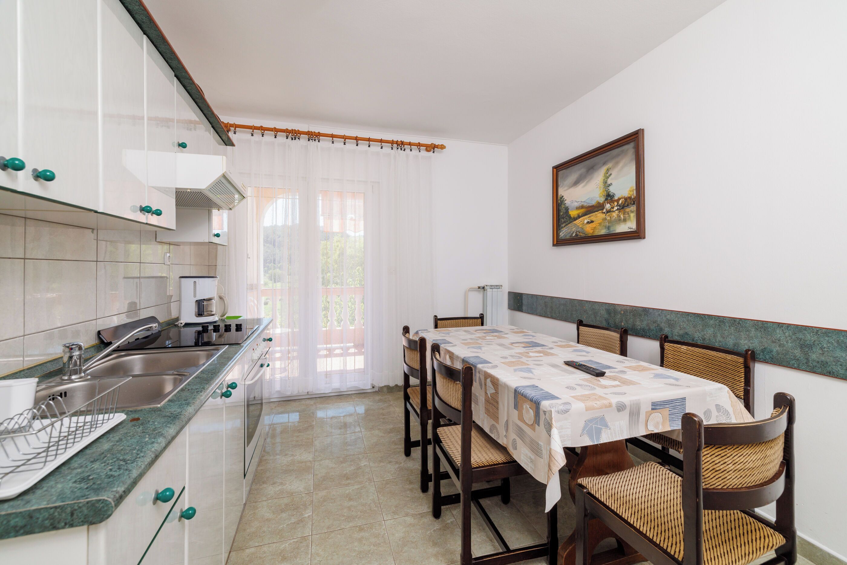A kitchen with a dining area, a painting on the wall, and a view through the window.