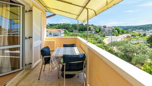A balcony with a table and chairs, a yellow awning, and a view of a town and greenery. - Apartments Marija I (Lopar)
