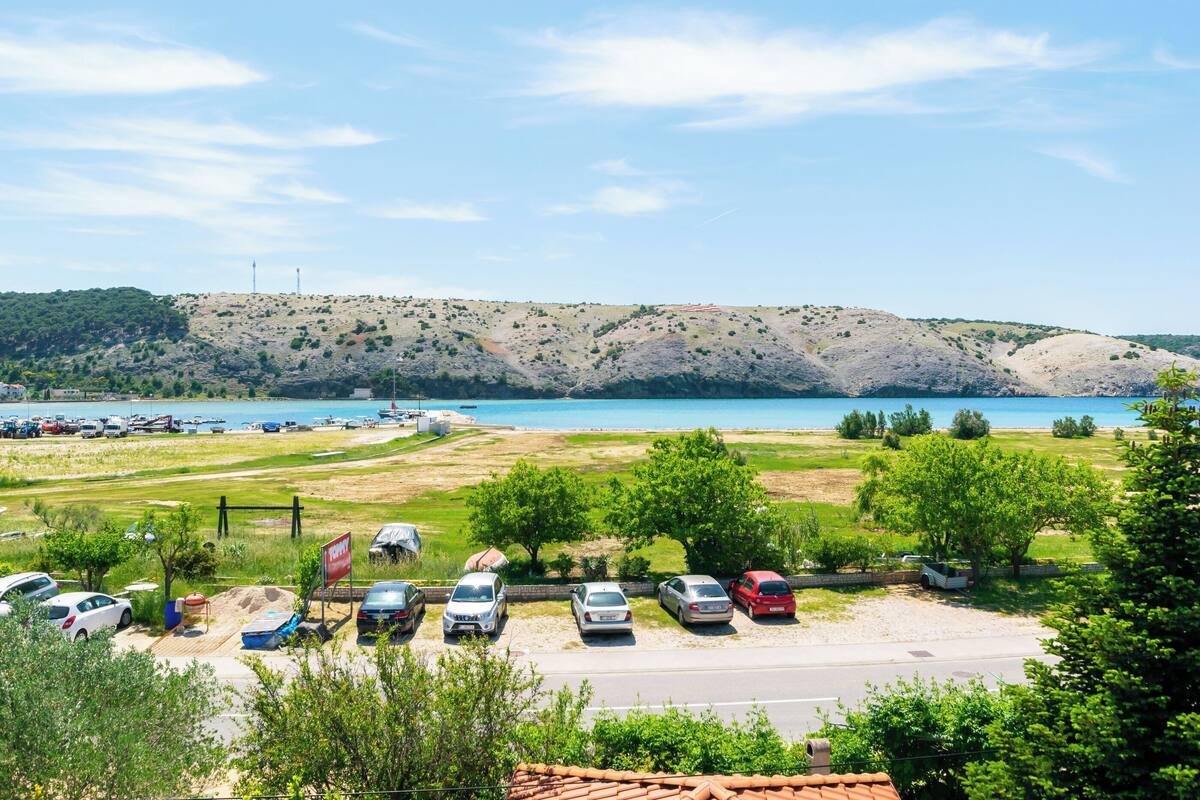 A parking area with cars, a beach, and a hilly landscape in the background.