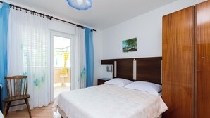 A bedroom with a bed, wooden wardrobe, and a chair. - Apartments Marija I (Lopar)