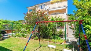 A residential area with a swing set in a garden, a parked car, and a building with balconies. - Apartments Marija I (Lopar)