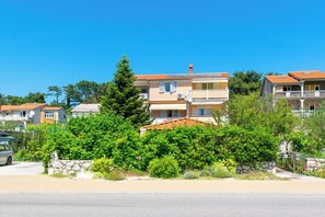 A residential building with multiple balconies, a stone wall, and lush greenery. - Apartments Marija I (Lopar)