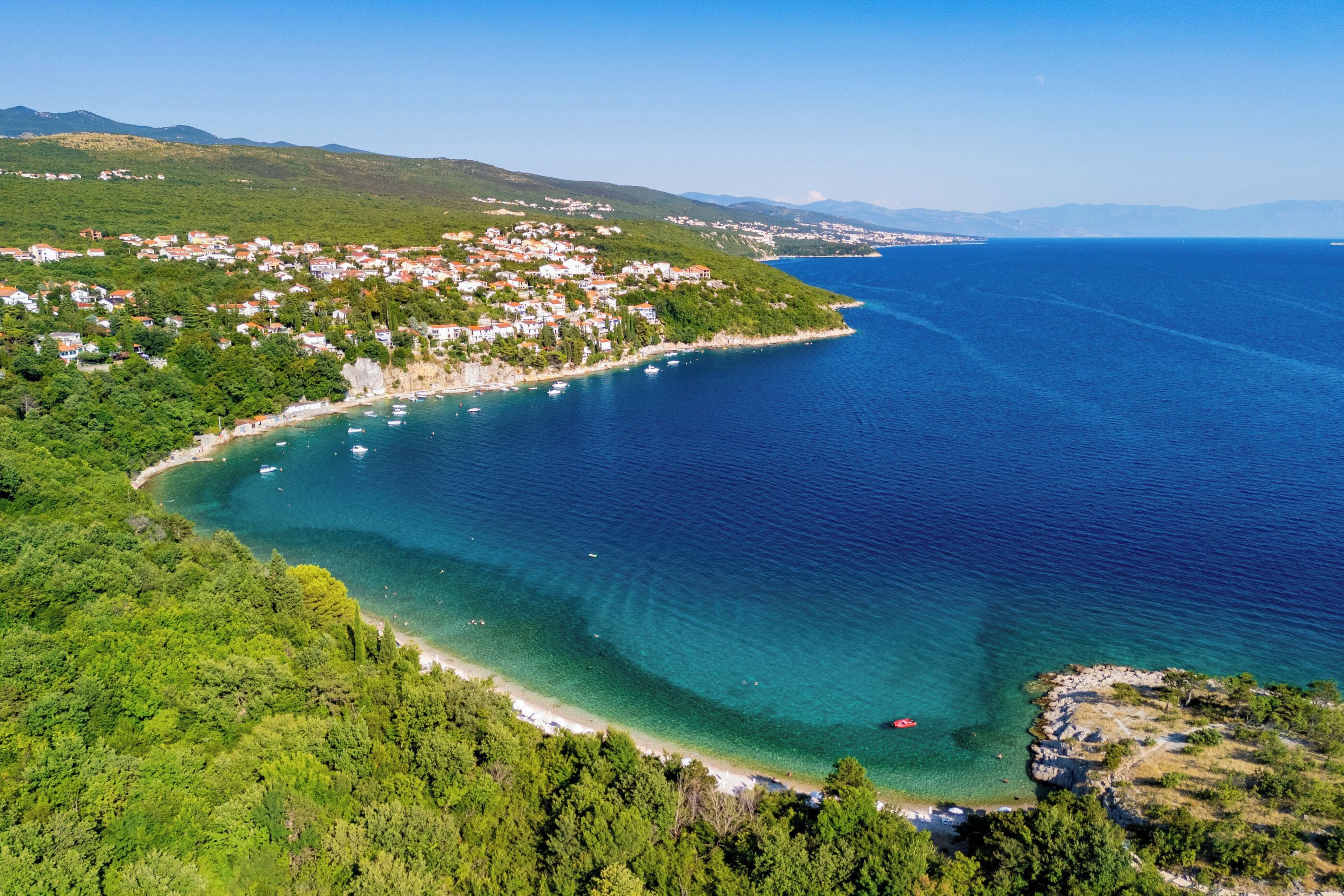 A coastal town with a clear view of the sea, a sandy beach, and lush greenery.