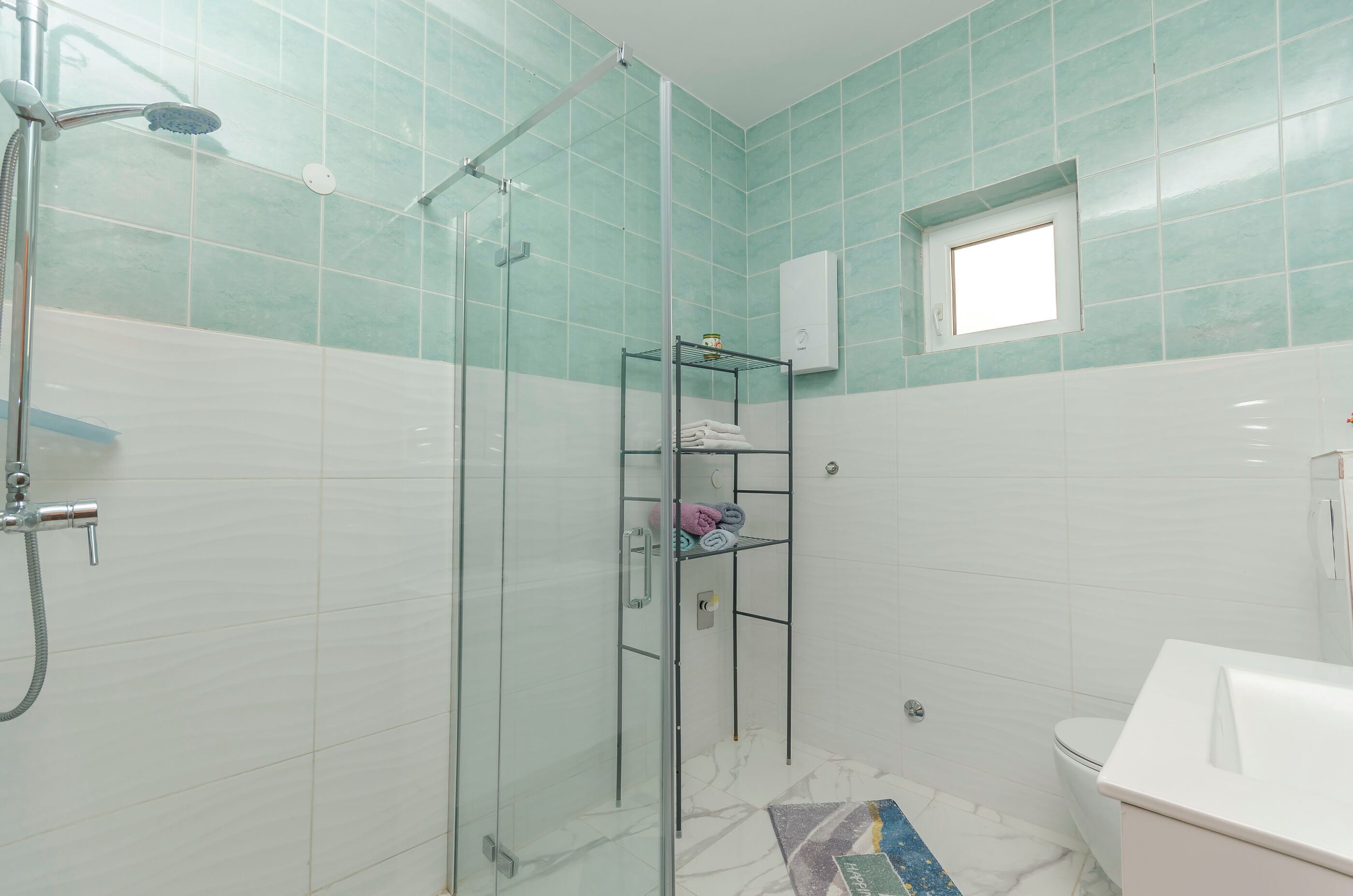 A bathroom with a glass-enclosed shower, a white sink, and a small window.