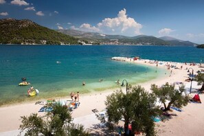 Une plage à l’eau turquoise et limpide, où l’on peut voir des gens nager et prendre des bains de soleil, et un petit bateau sur l’eau.