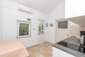 A small kitchenette with a stove, sink, and window. There is a door with a green exit sign and a window with a view of trees. - Apartments Mirjana (Marina)
