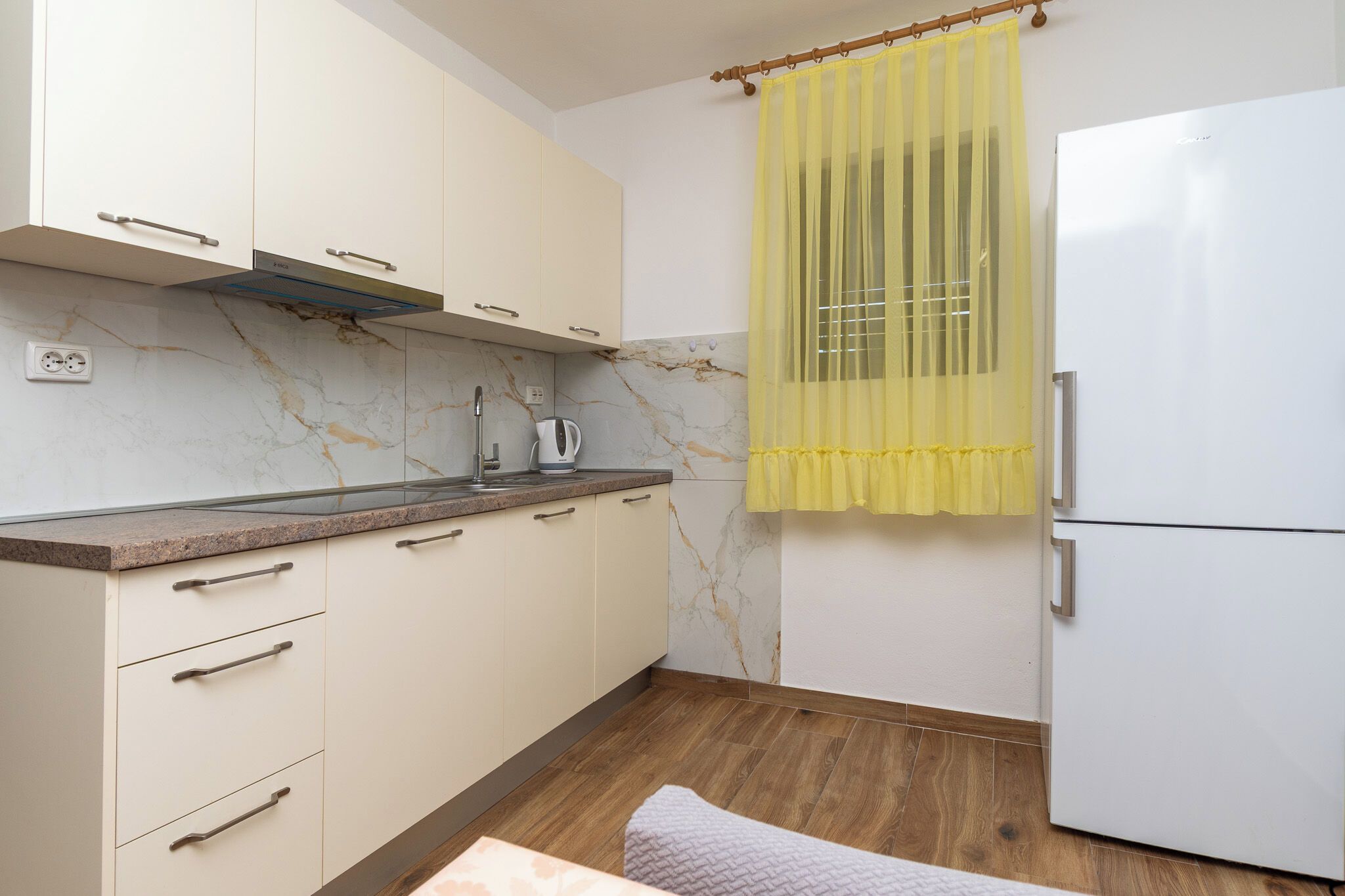 A kitchen with marble backsplash, a white refrigerator, and a yellow curtain.