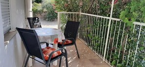 En udendørs terrasse med et bord og stole, omgivet af et hvidt gelænder og frodigt grønt.