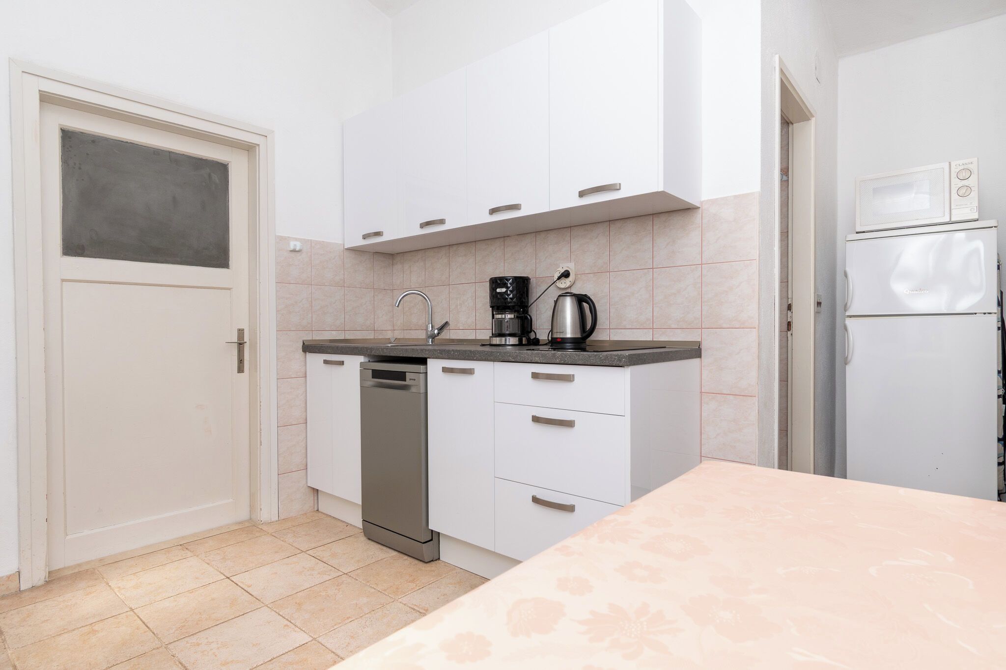 Een kleine keuken met witte kastjes, een vaatwasser, een koffiezetapparaat en een magnetron.
