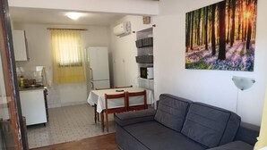 Et opholdsområde med sofa, spisebord med stole, et køkken med køleskab, og et billede af en skov.