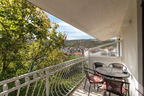 Un balcon avec une table et des chaises, donnant sur un quartier résidentiel et des arbres.