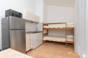 Une petite cuisine équipée comprenant un réfrigérateur, une cuisinière et des placards. On y trouve également un lit superposé avec une structure en bois et un matelas blanc.